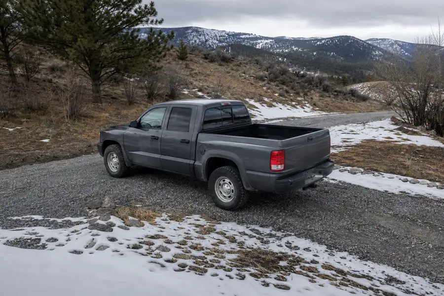Pickup truck on a gray gravel driveway during a Colorado spring thaw with patches of snow