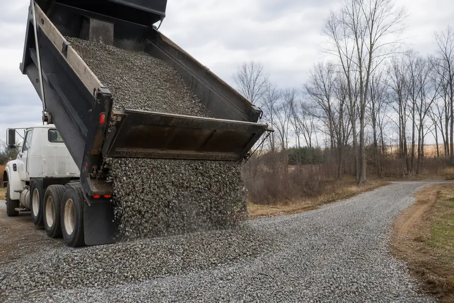 Dump truck tipping a load of crushed gravel onto a long rural driveway