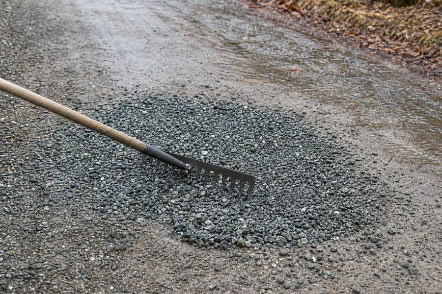 Landscape rake smoothing fresh gravel into a pothole on a rural driveway