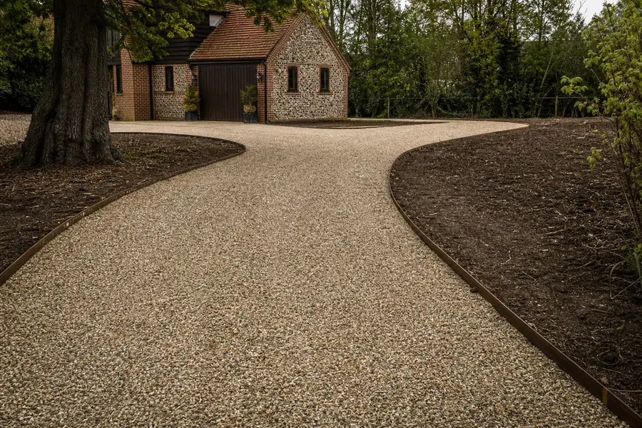 Finished crowned gravel driveway curving toward a house with wooden edging