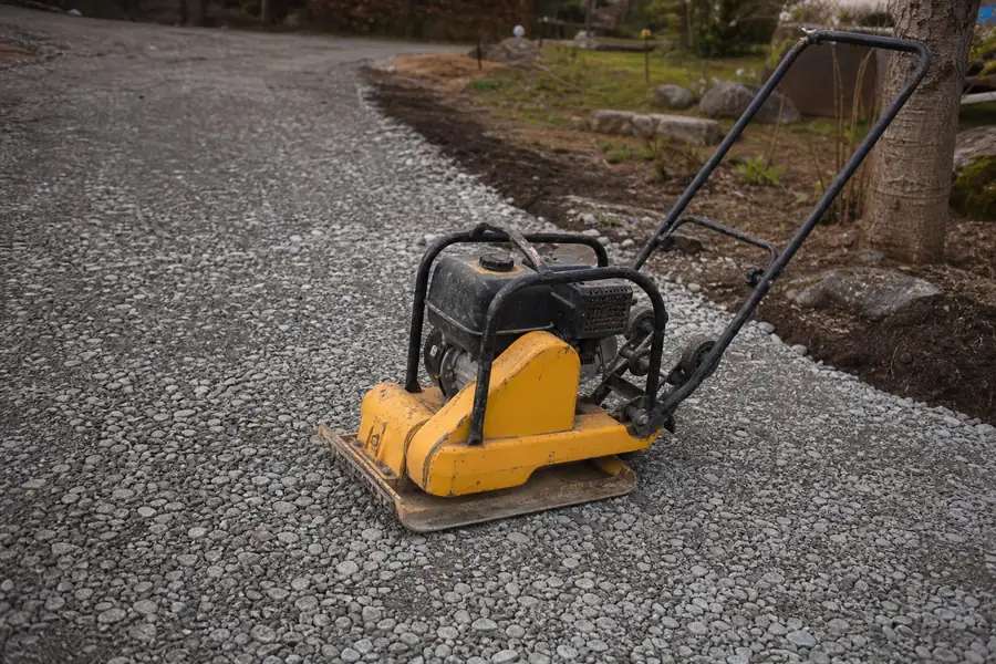 Plate compactor packing crushed stone on a new gravel driveway