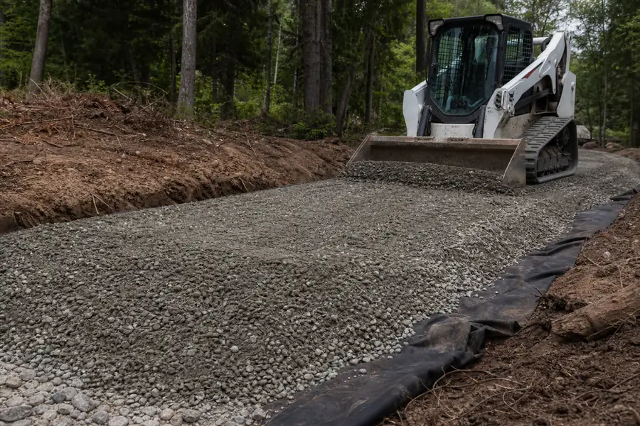 Skid steer spreading road base on an excavated driveway with geotextile fabric visible at the edge